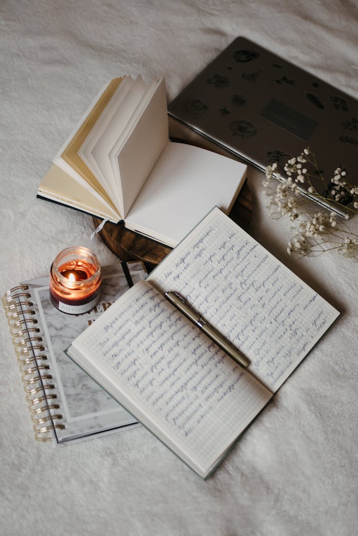 Services-02 A serene writing setup featuring notebooks, a lit candle, and a laptop in a cozy indoor setting.